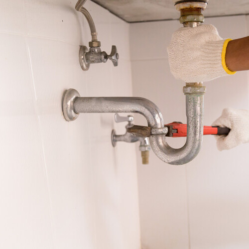 Plumber fixing white sink pipe with adjustable wrench.