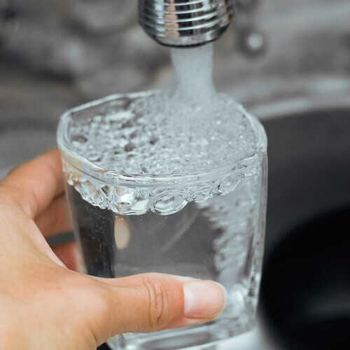 A stream of water flows into a glass cup close up